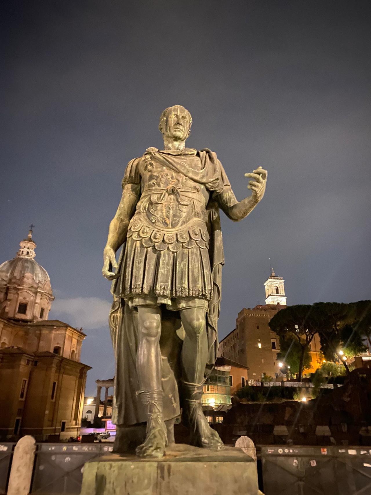 A bronze statue of Julius Caesar stands prominently at night.