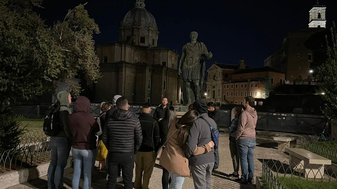A group of people gathered at night near a large statue and historical buildings.