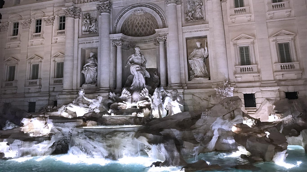 The image shows the illuminated Trevi Fountain at night.